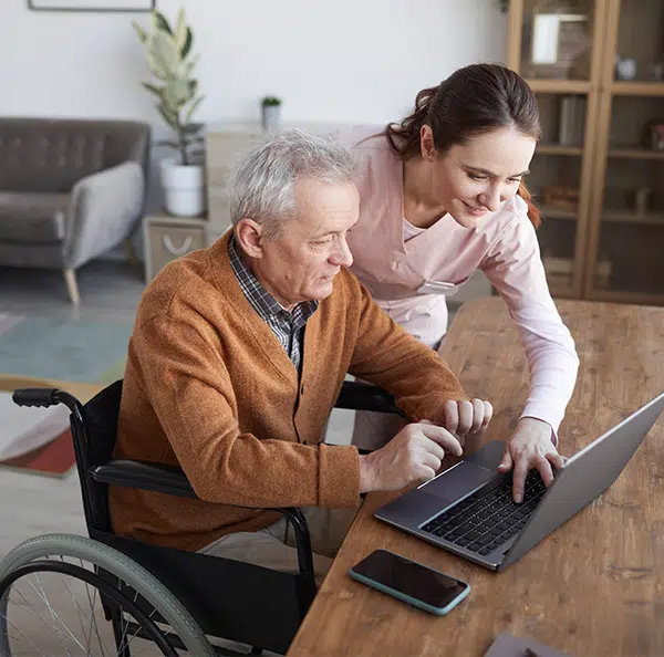 young woman helping older man in wheelchair to use a laptop computer